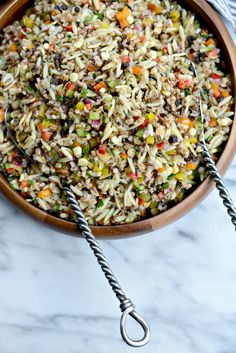 a bowl filled with rice and vegetables on top of a marble counter next to two tongs