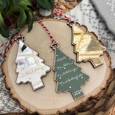 three christmas tree ornaments are sitting on a wood slice