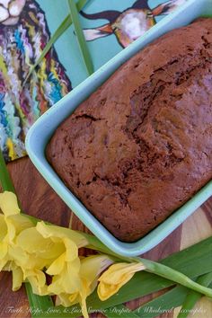 a loaf of chocolate cake sitting on top of a wooden table next to yellow flowers