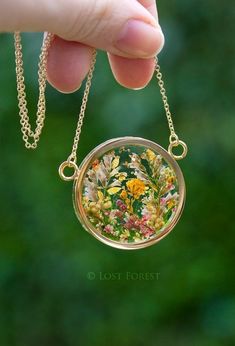 a hand holding a small glass pendant with flowers on it's chain, in front of a green background