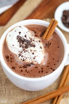 there is a cup of hot chocolate with whipped cream and cinnamon sticks on the side