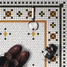 a pair of brown shoes sitting on top of a tiled floor next to a camera