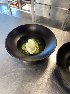 two black bowls filled with food on top of a metal counter