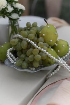 grapes and pears in a bowl on a table with pearls around the edges for decoration