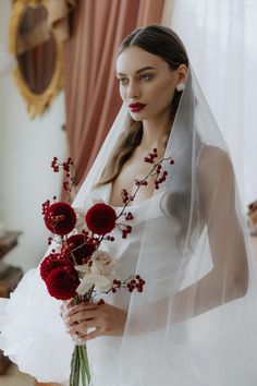 a woman in a wedding dress holding a bouquet of red flowers and wearing a veil