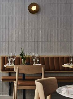 a restaurant with wooden tables and chairs next to a white tiled wall that has a round light above it