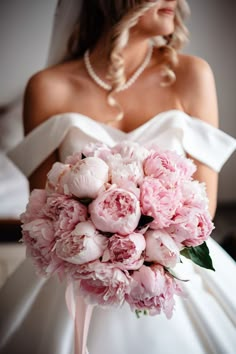 a bride holding a bouquet of pink peonies