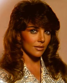 an old photo of a woman with long hair and blue eyes wearing a silver shirt