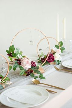 the table is set with white plates, goldware and floral centerpieces on it