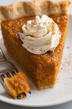 a slice of pumpkin pie with whipped cream on top and a fork next to it