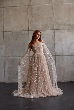 a woman with red hair wearing a beige dress and holding a long white veil in front of her face