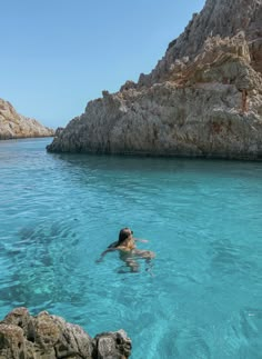 a person swimming in the blue water near some rocks and large rock formations on the shore