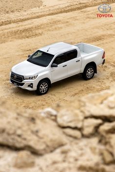 a white truck is parked in the middle of a dirt area with rocks and sand behind it