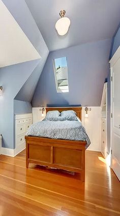 a bed sitting in the middle of a bedroom under a slanted skylight on top of a hard wood floor