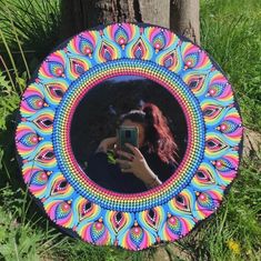 a person taking a photo in a colorful circular mirror on the ground next to a tree