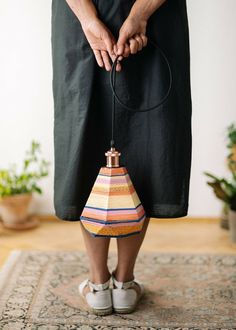 a woman is holding an object in her hands while standing on a rug with plants behind her