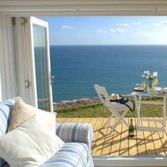 a table and chairs sitting on top of a wooden deck next to the ocean in front of an open door