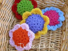 four crocheted flowers sitting on top of a wicker basket next to each other