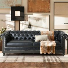 a black leather couch sitting on top of a wooden floor in front of pictures and paintings