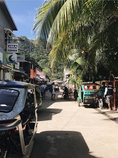 people are walking down the street in front of some parked cars and motorbikes