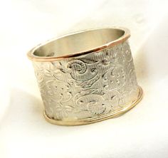 a silver ring with floral designs on it sitting on a white surface, in the middle of an image