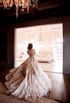 a woman in a wedding dress is looking out the door to her living room, with chandelier hanging from the ceiling