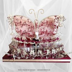 a pink and white butterfly shaped cake with wine glasses in it's wings on a table