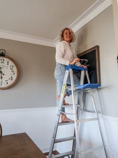 a woman standing on a ladder in front of a clock