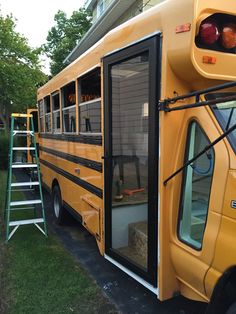 a yellow school bus parked in front of a house with its door open and ladder leaning against it