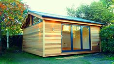 a small wooden building in the middle of a yard with trees and bushes around it