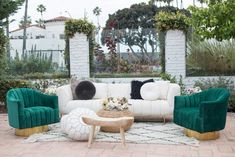 a living room with green velvet furniture and white brick flooring, surrounded by greenery