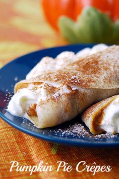 a blue plate topped with two crepes covered in whipped cream next to a pumpkin