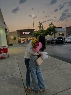 two people hugging each other on the side walk in front of a store at sunset