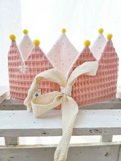 two pink princess crowns are sitting on a wooden bench with a ribbon tied around them