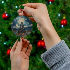 a person holding up a christmas ornament in front of a christmas tree with lights