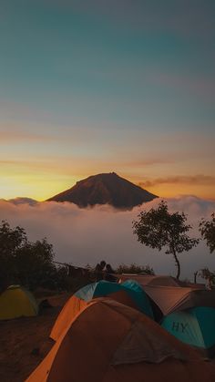 tents are set up on the top of a mountain with clouds in the sky behind them