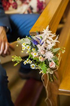 a bouquet of flowers sitting on top of a wooden bench next to a person's legs