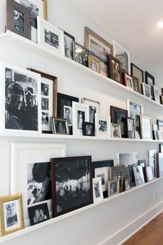 a wall filled with lots of framed pictures on top of white shelves next to each other