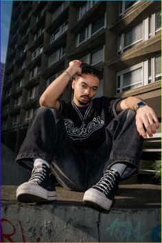 a young man sitting on the side of a wall with his hands in his hair