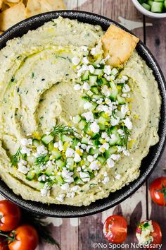 a bowl filled with hummus, cucumber and crackers next to tomatoes