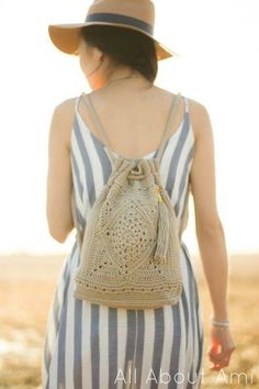 a woman wearing a striped dress carrying a crochet bag in the desert with her back to the camera