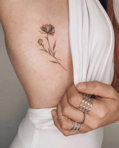 a woman with a flower tattoo on her back and arm, holding onto the side of her body