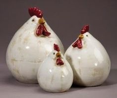 three ceramic chickens sitting next to each other on a gray surface with white and red accents