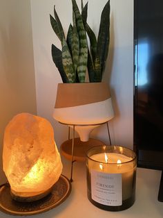 a candle next to a potted plant on a table with a lit candle in front of it