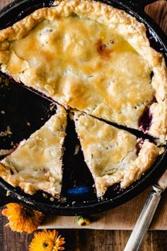 a pie sitting on top of a wooden cutting board next to a knife and flowers