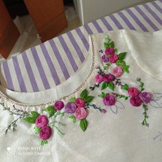 a white shirt with pink flowers on the front and green leaves on the back, sitting on a striped table cloth