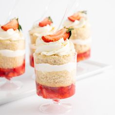 three desserts with strawberries and whipped cream in small glass dishes on a white surface