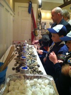 several people standing around a long table filled with rocks and marshmallows on it