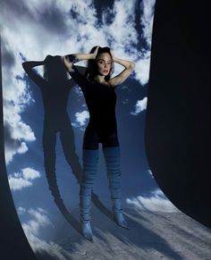 a woman standing in front of a giant shadow with her hands on her head and arms behind her head