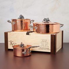 two copper pots and pans sitting on top of a wooden box next to each other